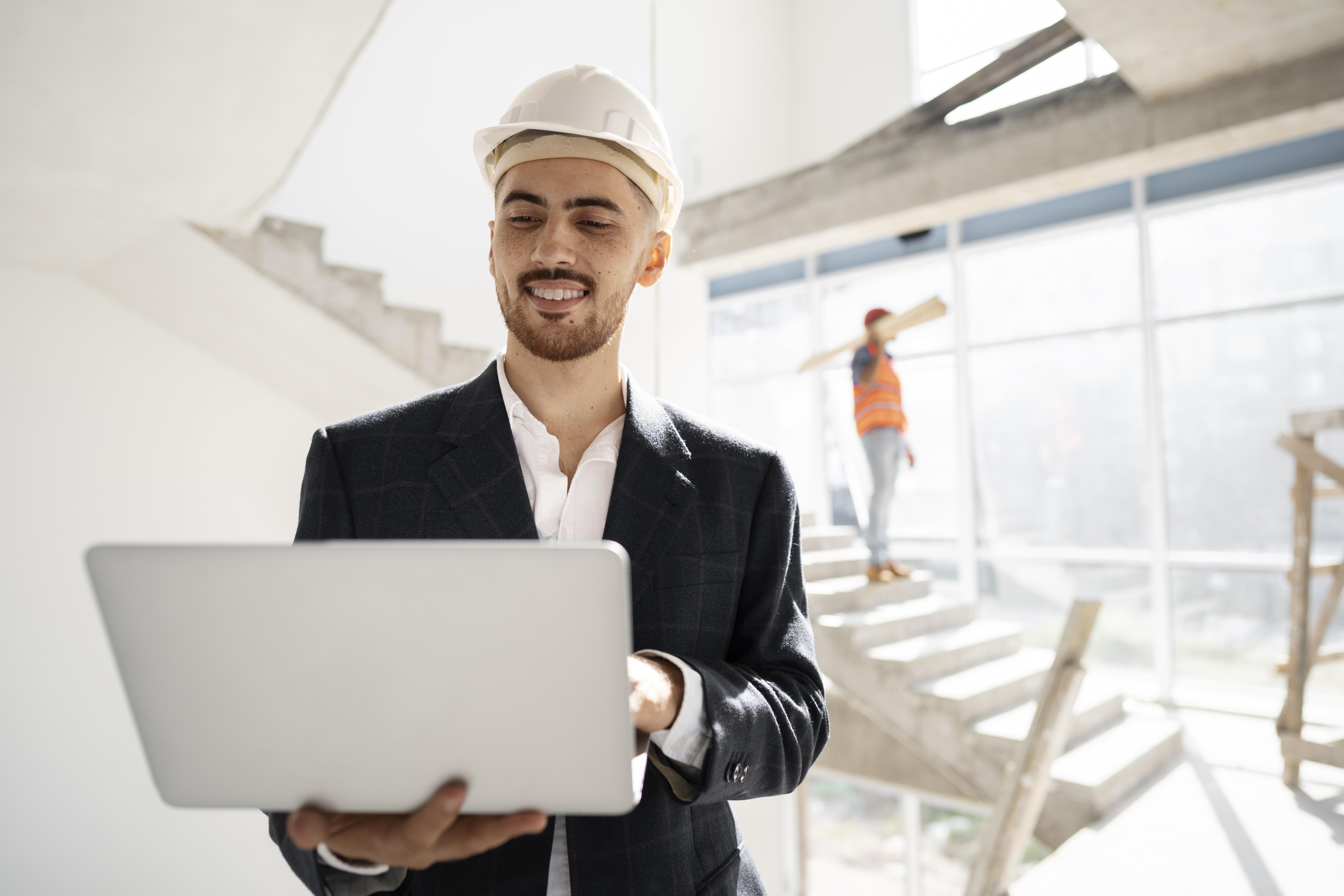 Smiling architect in hard hat using laptop at construction site