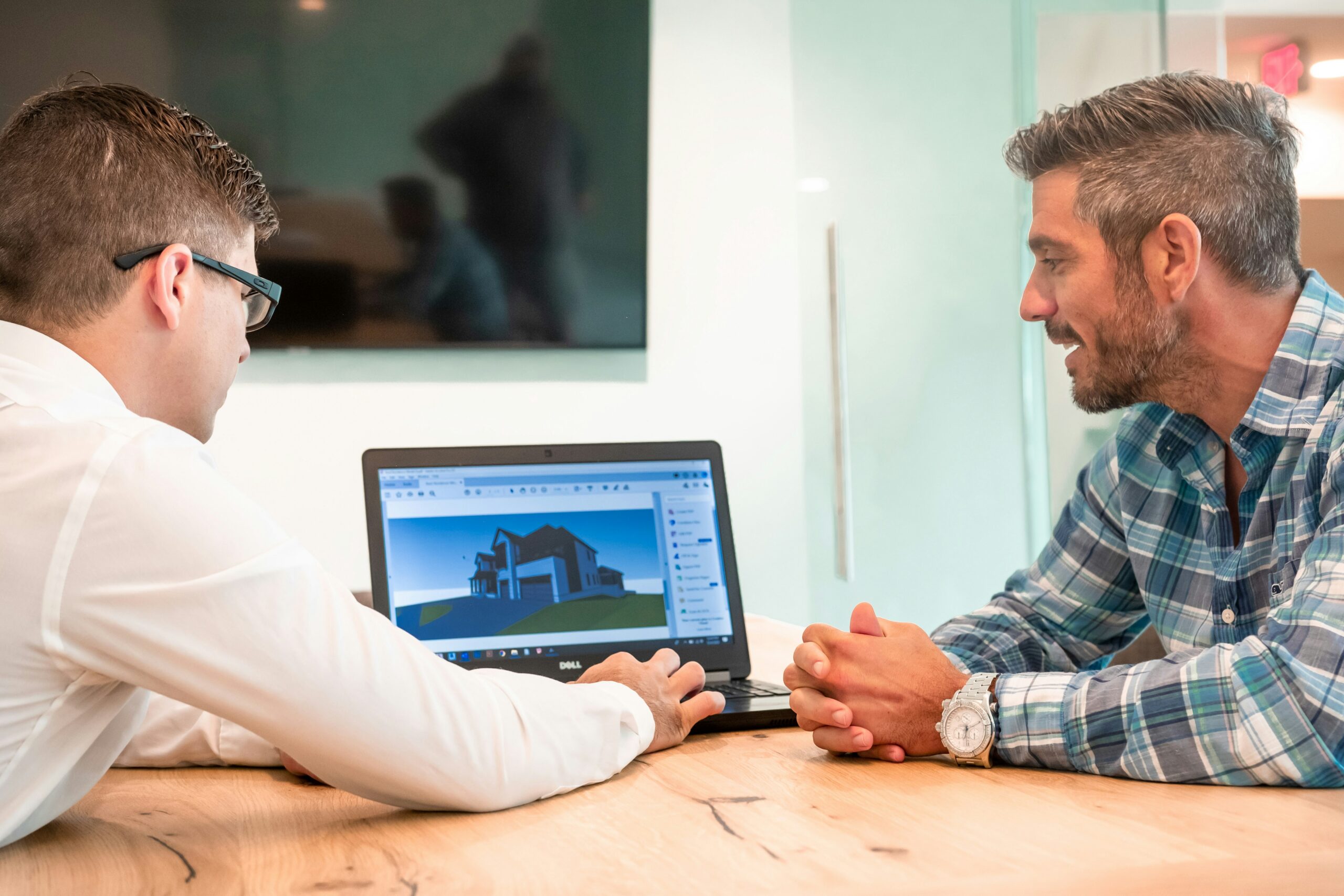 Two architects discussing a 3D house model on a laptop
