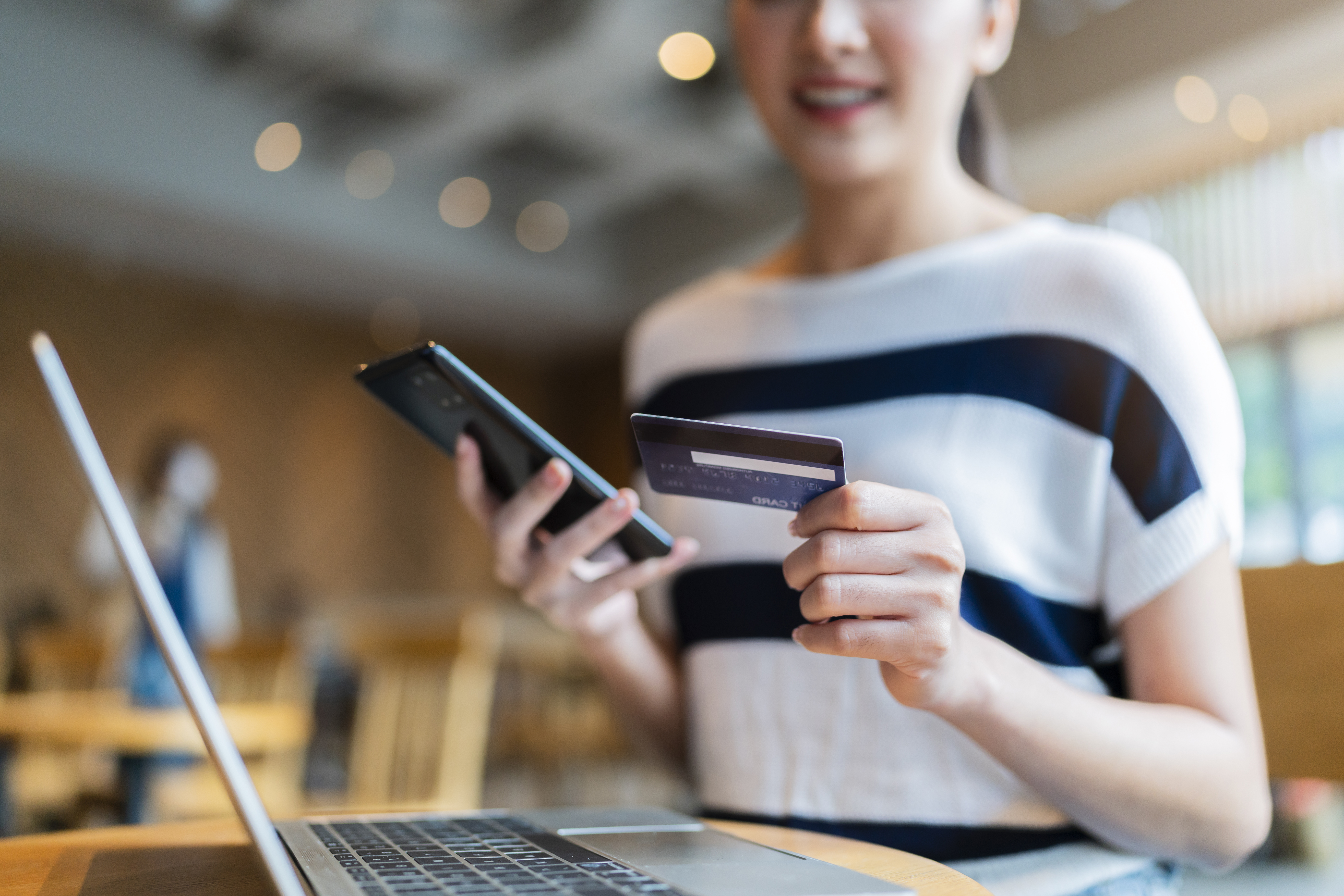 Woman holding a credit card and a phone in front of laptop