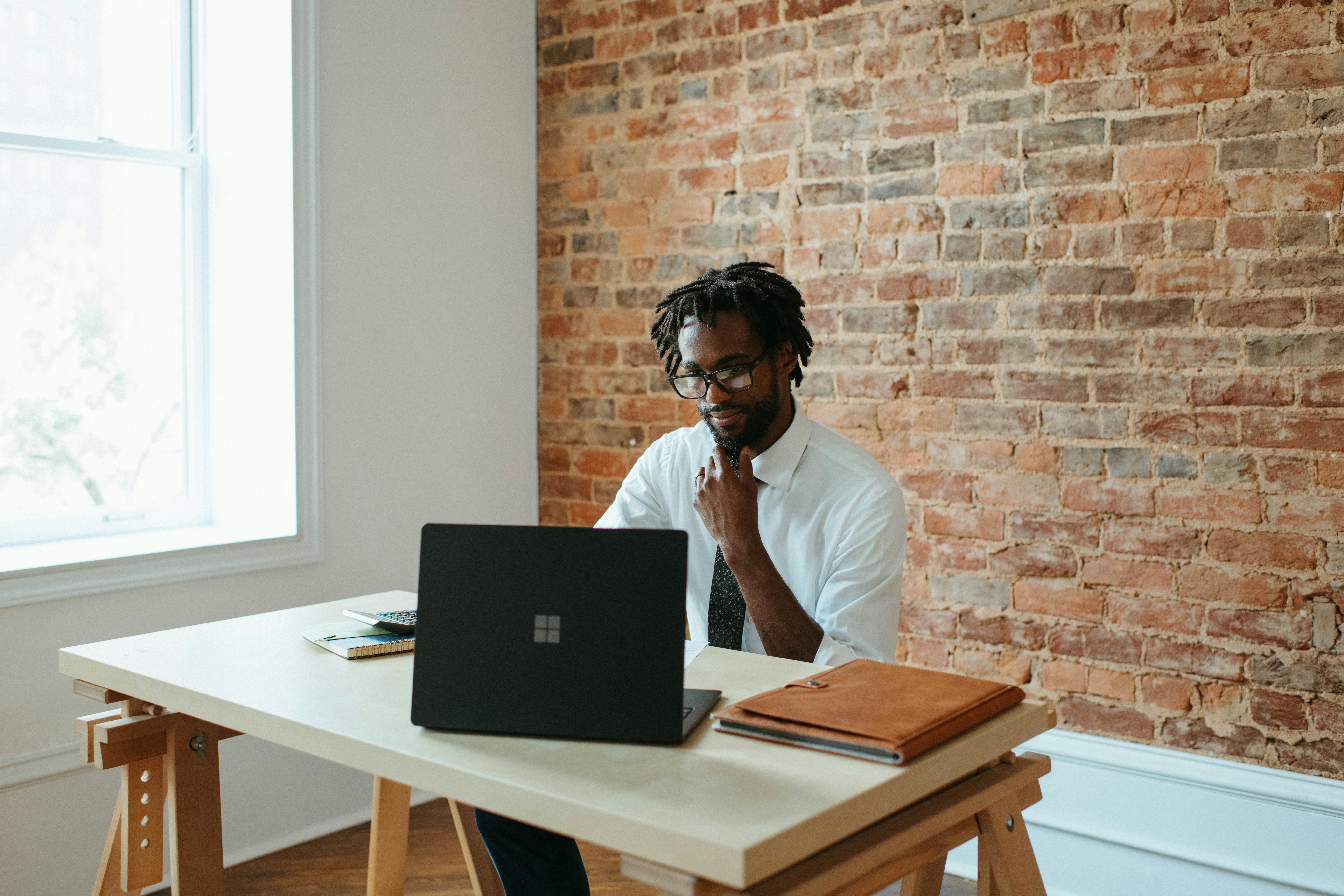 Man working in a brick office with a Microsoft laptop.