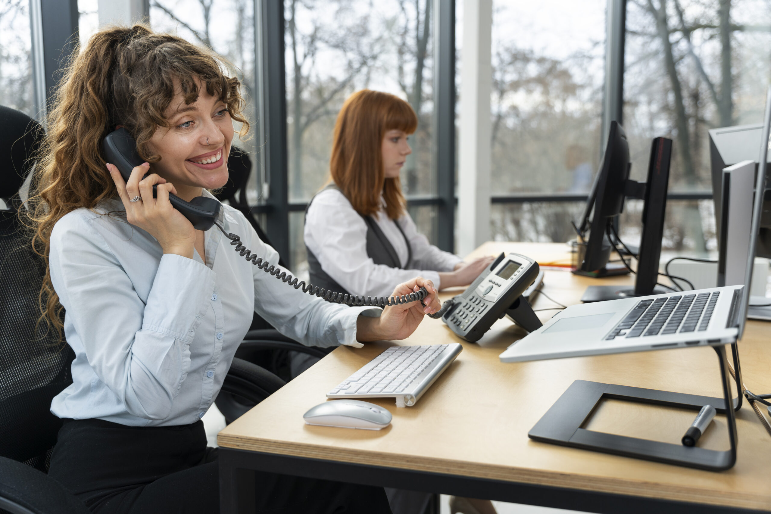 Smiling office worker using VoIP phone at work station