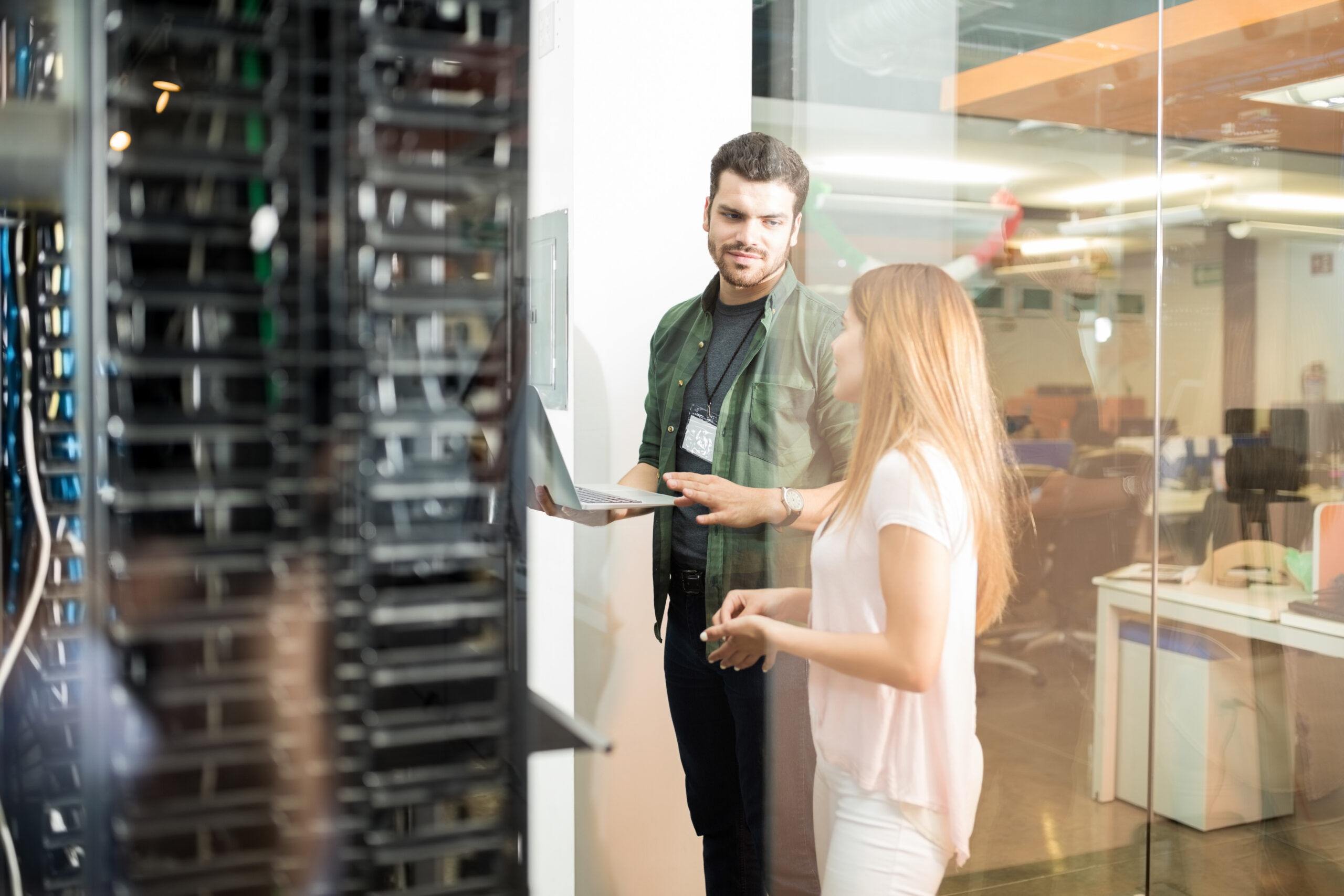 Two IT professionals discussing work beside a server room.