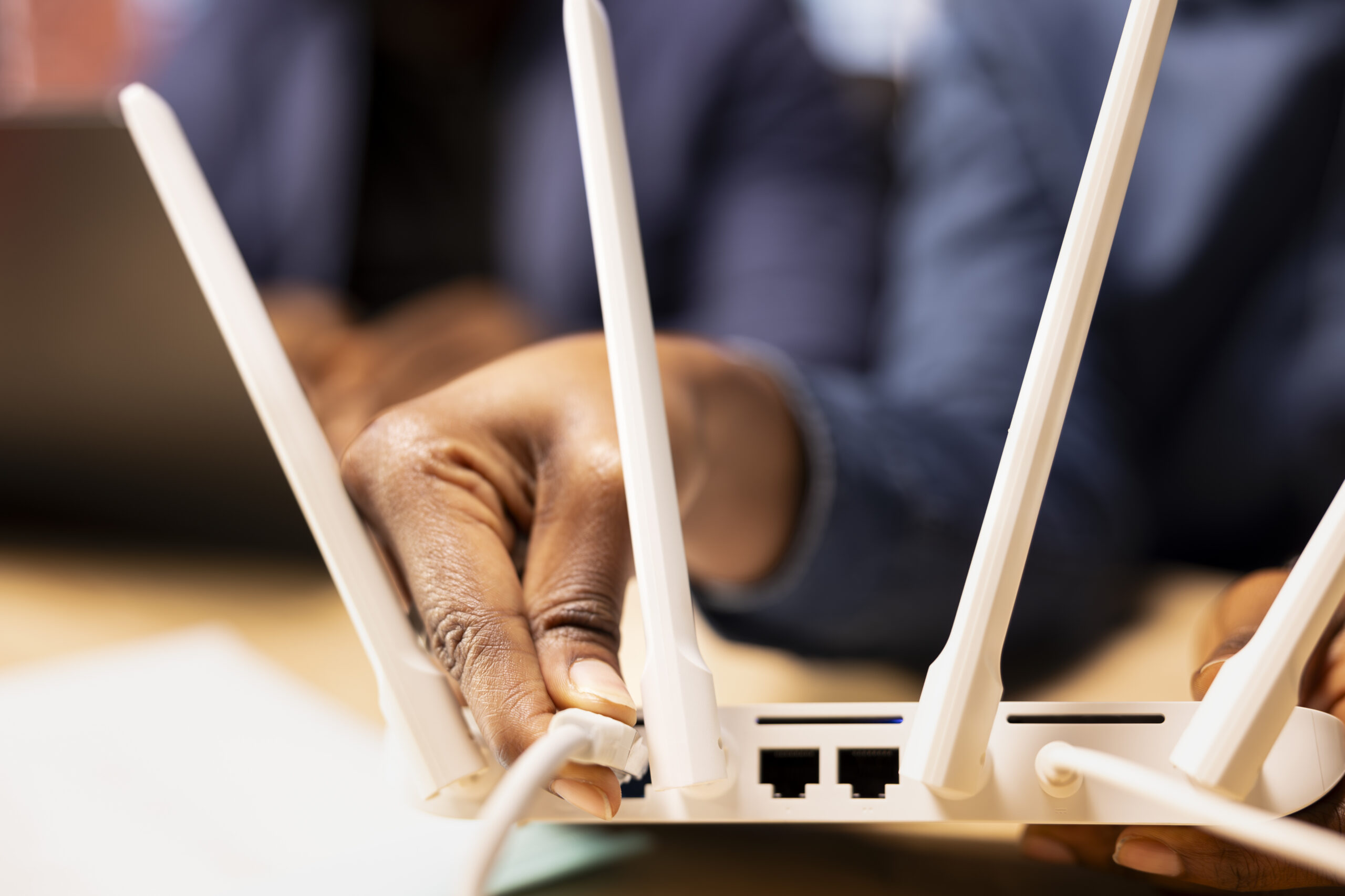 Hand plugging a cable into a white Wi-Fi router.